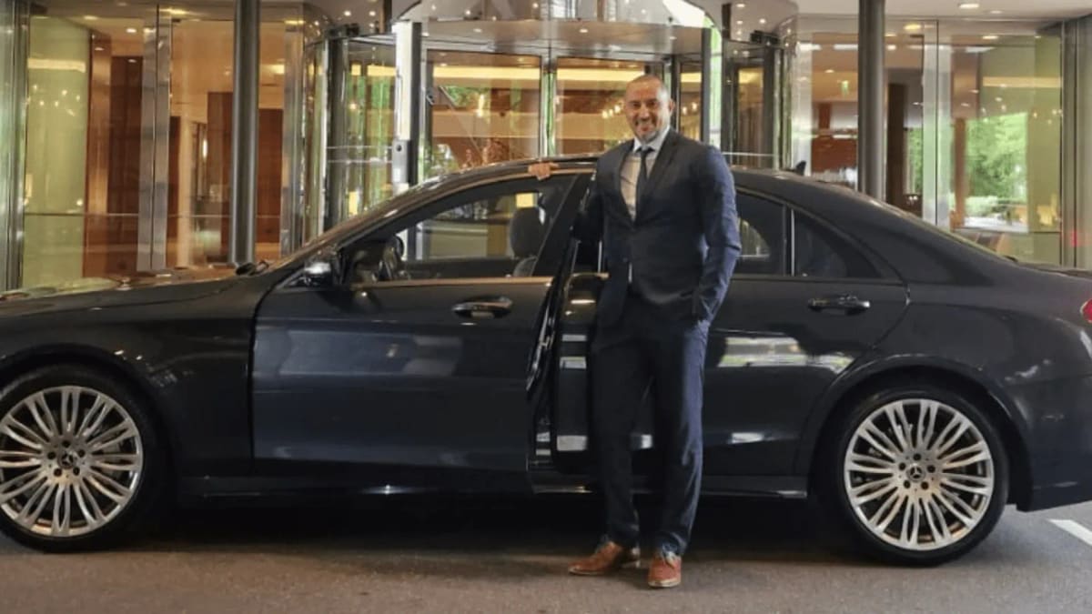 Chauffeur van Deluxe Taxi Holland bij de geopende deur van een Mercedes S-Klasse voor een hotel